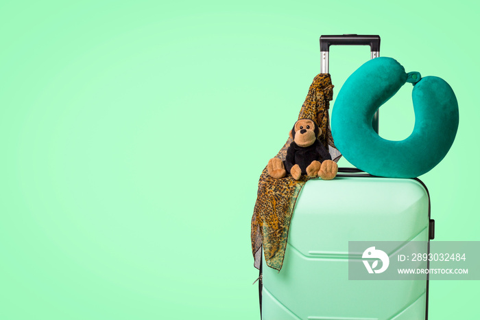 带轮子的塑料行李箱，软玩具，旅行枕头，颈巾，绿色背景。trav的概念