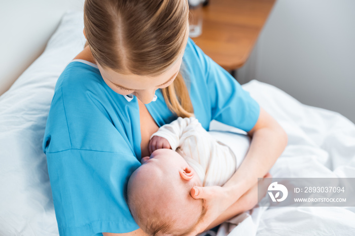 high angle view of young mother breastfeeding baby on bed in hospital room