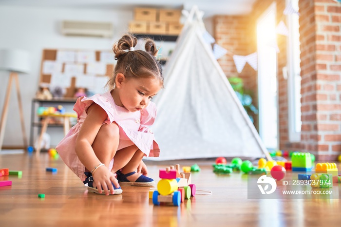 幼儿园里，年轻漂亮的蹒跚学步的孩子坐在地板上玩木制火车玩具