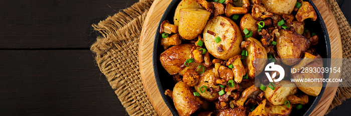 Baked potatoes with garlic, herbs and fried chanterelles in a cast iron skillet. Banner. Top view