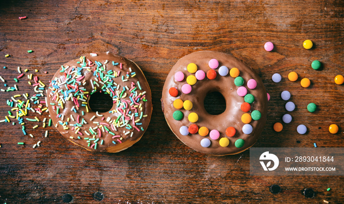 Donuts with chocolate glaze, sprinkles, two, top view and isolated, wooden background.