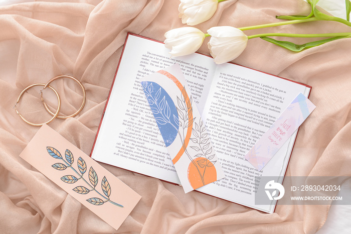 Book with bookmarks and flowers on color background