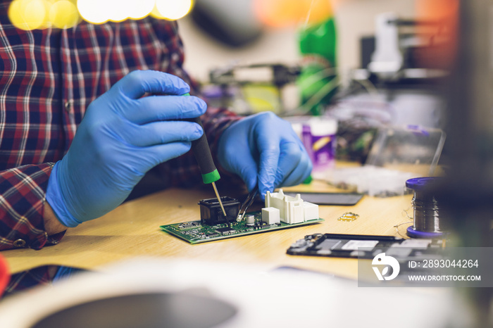 Technician engineer in workshop. Repairman is checking circuit board of electronic device.