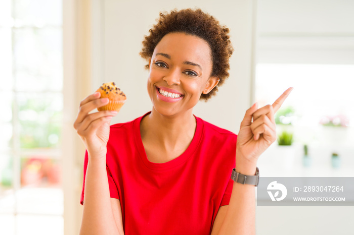 Young african american woman eating chocolate chips muffins very happy pointing with hand and finger