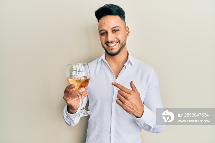 年轻的阿拉伯男子喝着一杯白葡萄酒，面带微笑，用手和手指指指点点