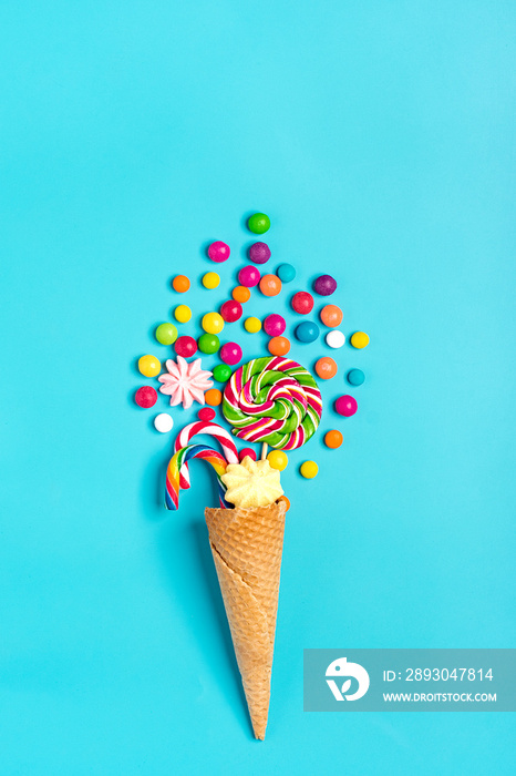 mix colorful chocolate sweets spilled out of ice cream waffle cone on blue background Flat lay Top v