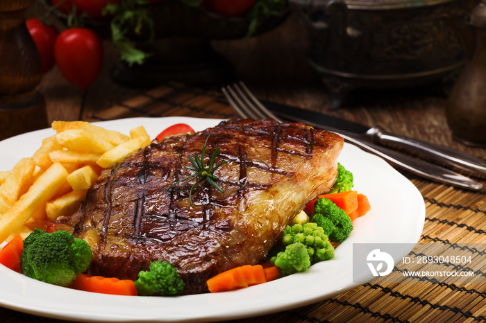 Grilled beef steak served with French fries and vegetables on a white plate.