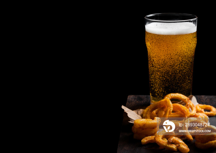 Glass of lagger beer with curly fries snack on vintage wooden board on black background. Space for t