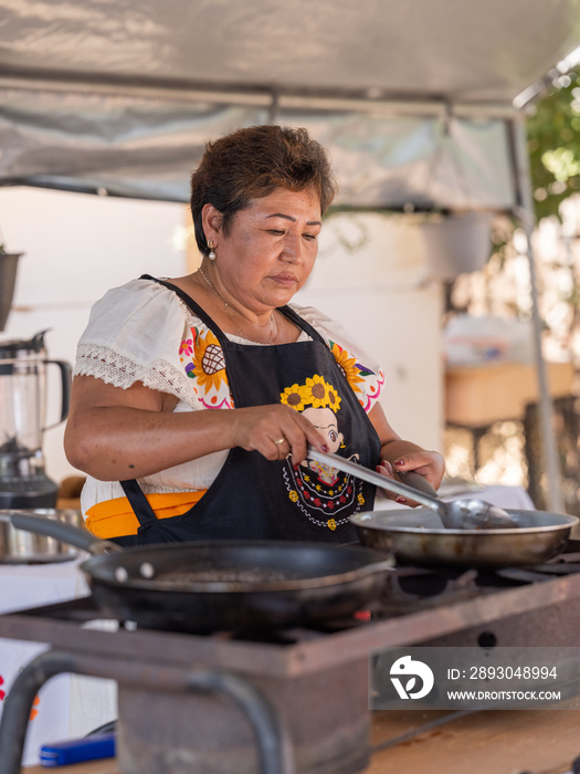 Vertical wide-image of an Indigenous woman frying food in a pan