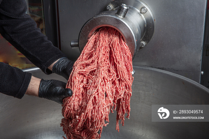 Unidentifiable butcher holding tray full of minced raw red meat leaving machine in food processing p