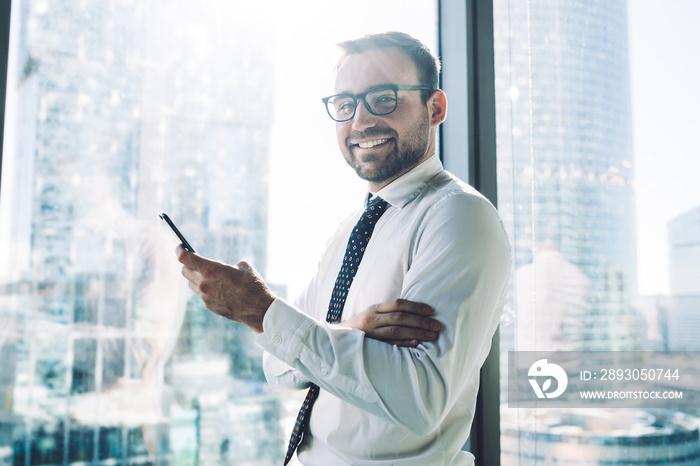 Half length portrait of cheerful male trader in white shirt looking at camera while waiting for sms 