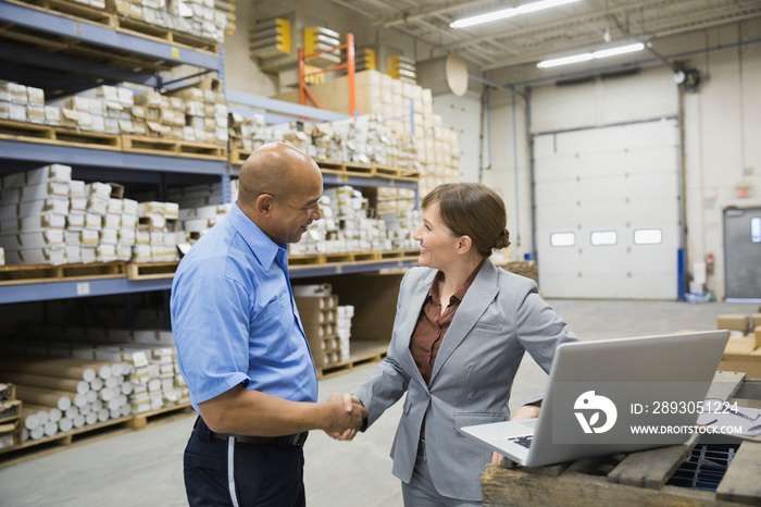 Manager and worker shaking hands in warehouse