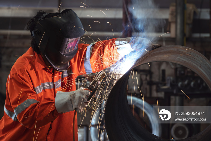 A Worker with protective mask welding metal pipe in a factory