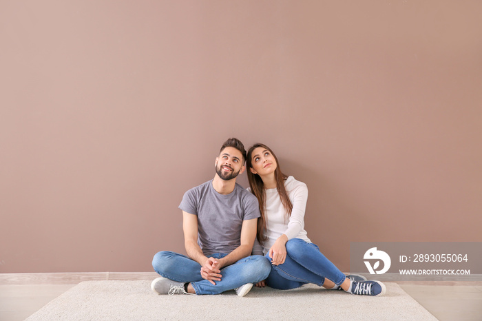 Young couple sitting near color wall