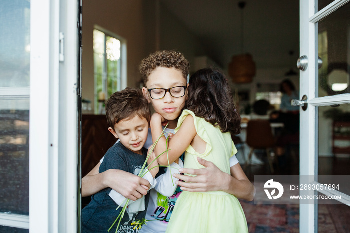 Siblings embracing while standing at home seen through window