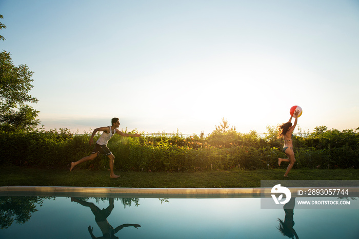 Side view of man running after woman poolside