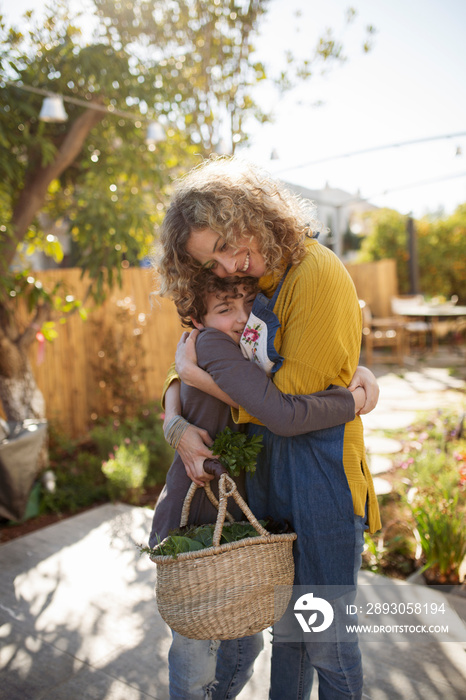 Side view of smiling mother embracing son while standing on footpath against sky in yard