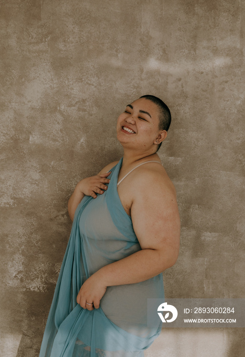 portrait of a plus size filipino woman with shaved head wrapped in blue fabric smiling