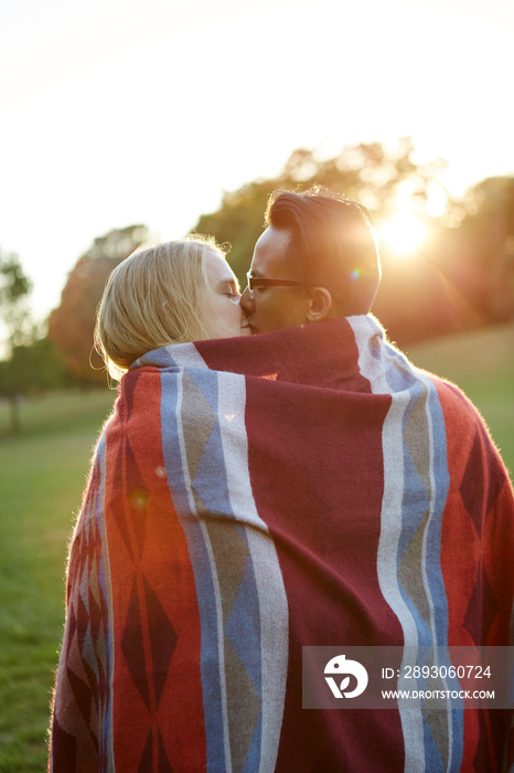 情侣裹着毯子，在阳光明媚的公园接吻