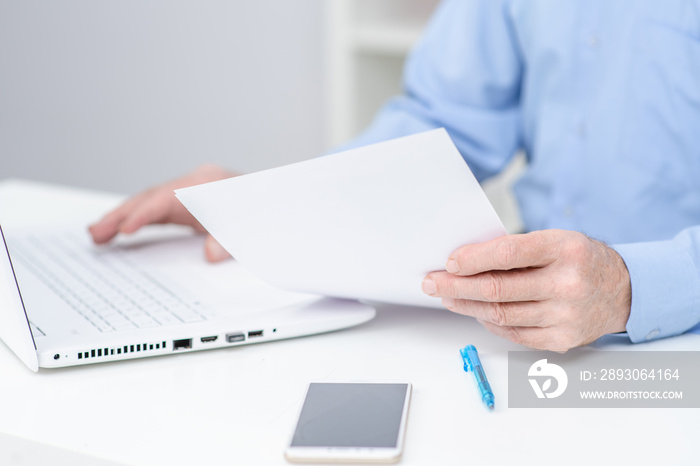 Senior man reads document and works on laptop in the office