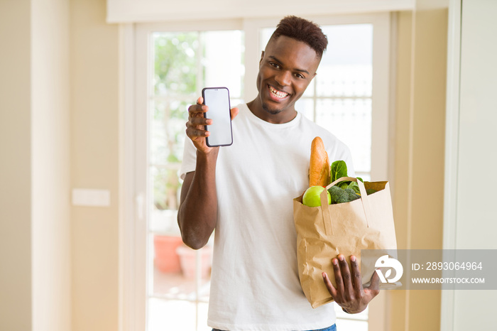 African man holding a paper bag full of groceries and using smarpthone buying online using app smili