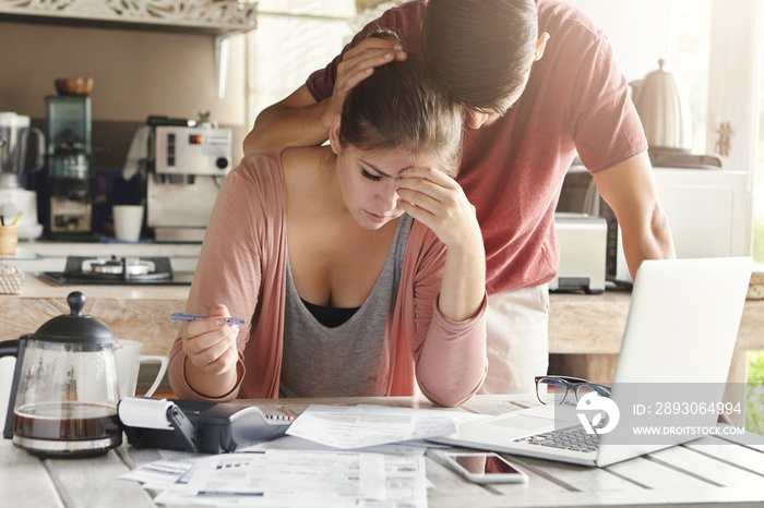 Unhappy couple unable to pay loan on time: stressed female doing paperwork sitting at table with lap