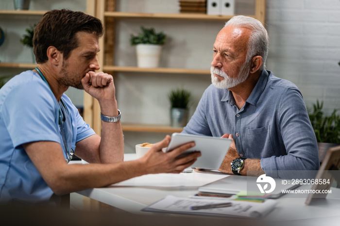 Senior man talking to a doctor who is using touchpad during medical appointment.