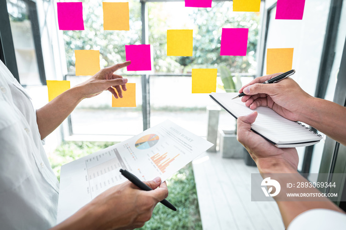 Young creative team professional using post it notes in glass wall to writing strategy business plan