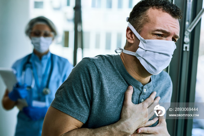 Man with face mask having chest pain and coughing while being at medical clinic.