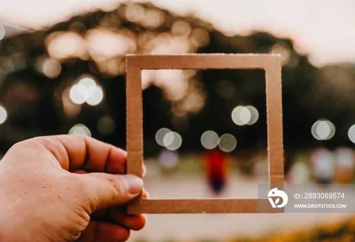 Hand holding blank paper frame with nature bokeh background