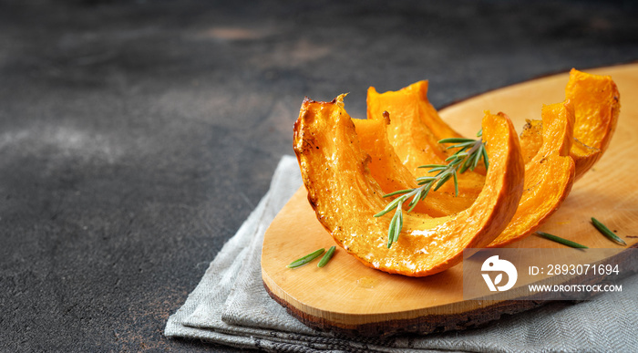 Slices of roasted pumpkin on wooden tray and dark background