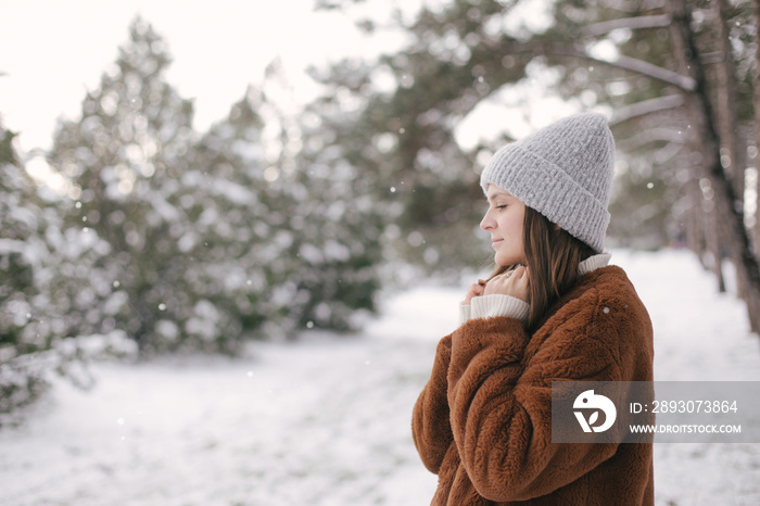 穿着人造毛皮大衣，戴着羊毛帽的女人正在享受降雪。