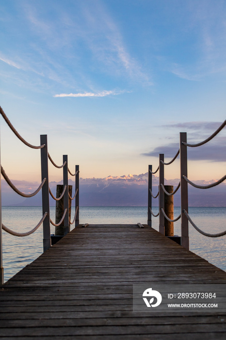 Ponton en bois ouvrant sur les Alpes enneigés sur les berges du Lac Léman à Morges au coucher du sol