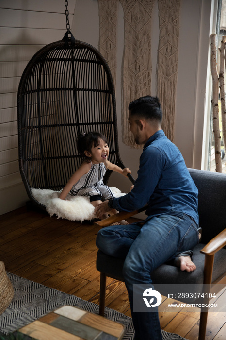 Side view of father talking to cute daughter sitting on swing at home