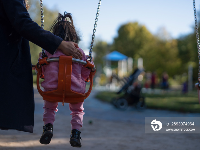 Mother swinging daughter on playground swing