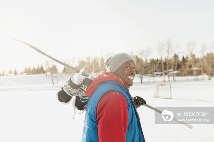 Smiling man walking with ice skates and hockey stick