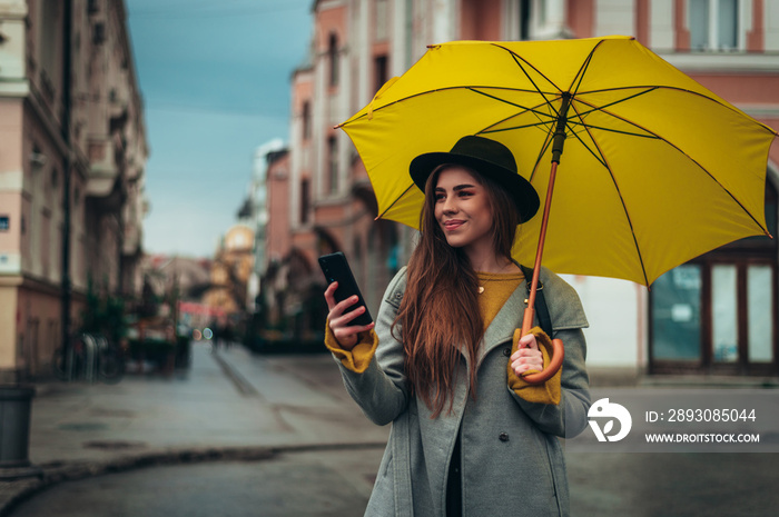 一名女子在外面拿着黄色雨伞使用智能手机