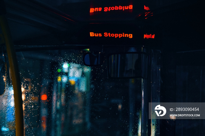 Bright orange Bus Stopping sign in night public transport, blurred street lights visible behind glas