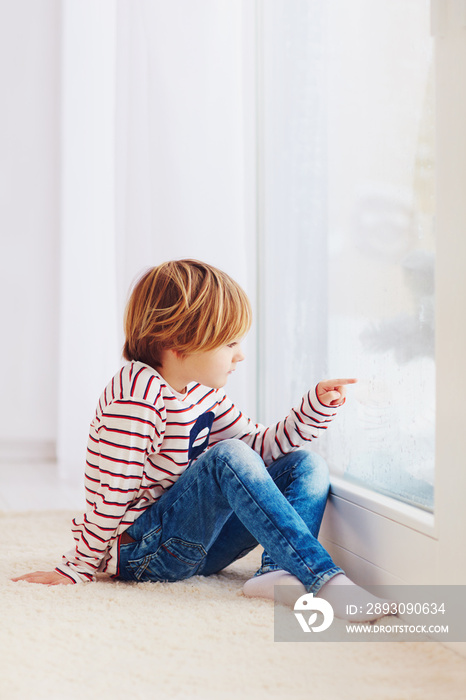 雨天坐在靠近窗户的地毯上的英俊小男孩