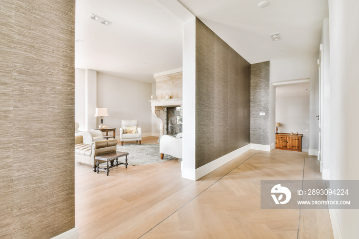 A wide corridor covered with brown wallpaper and an arch leading to the living room