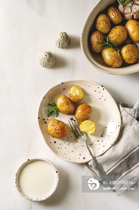 Young baked potatoes with garlic and rosemary in ceramic plate and baking dish, served with cheese s