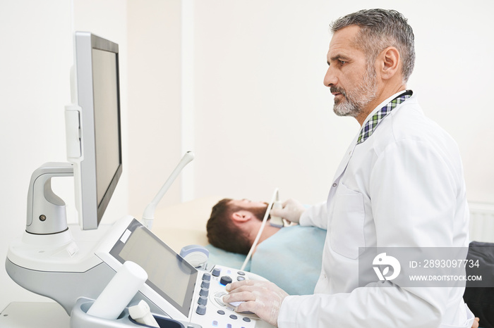 Doctor sitting, looking at screen, doing diagnosis of neck.