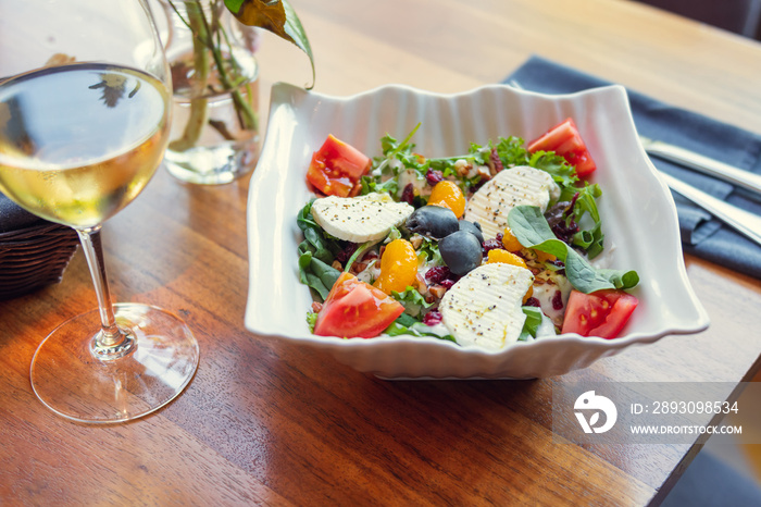 餐厅餐桌上的沙拉配一杯白葡萄酒。奢华的日光健康食品理念