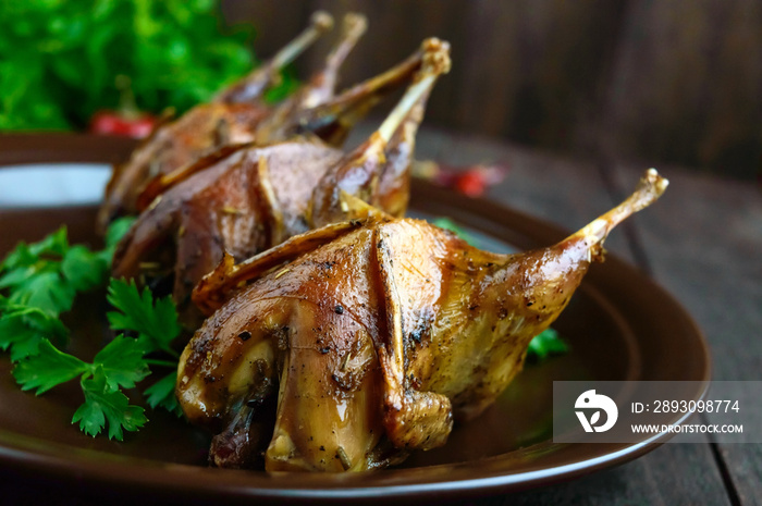 Roasted quail on a spit. Serving on a ceramic plate with greens. Close-up. Holiday menu.