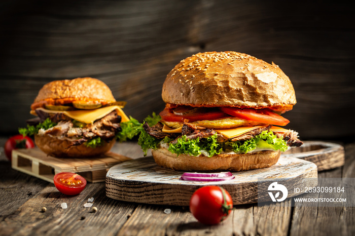 Homemade burger with grilled beef meat, vegetables, sauce on rustic wooden background. fast food and