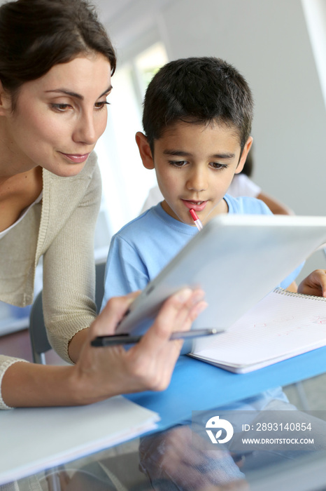 Teacher and schoolboy using electronic tablet in class