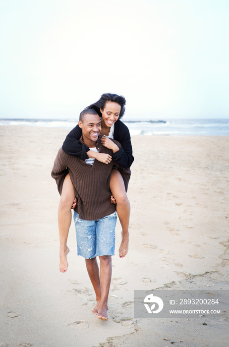 Young man carrying girlfriend on his back on beach