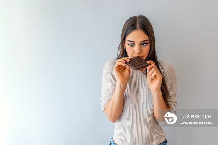 Portrait of young woman with chocolate bar on grey background. Portrait of a hungry pretty girl biti