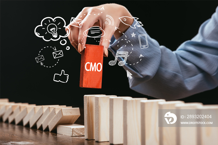 cropped view of woman picking red block with word cmo out of wooden bricks, icons on foreground