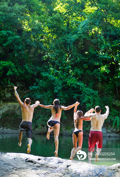 Four friends holding hands and jumping into lake